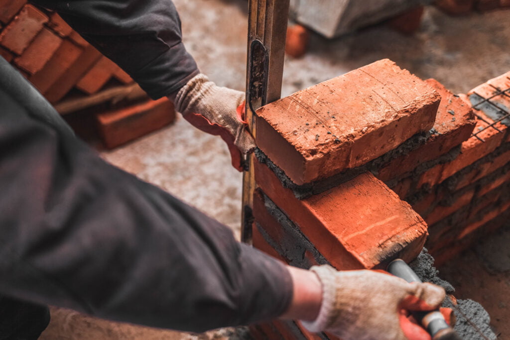 Bricklayer puts bricks to make a wall