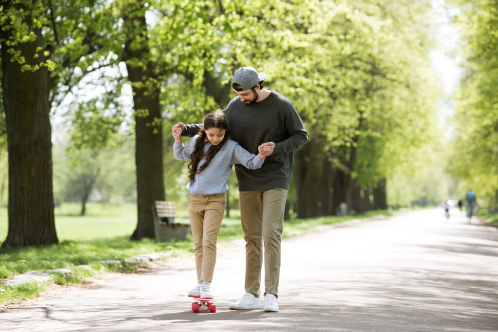 father helping daughter to ride on skateboard in park
