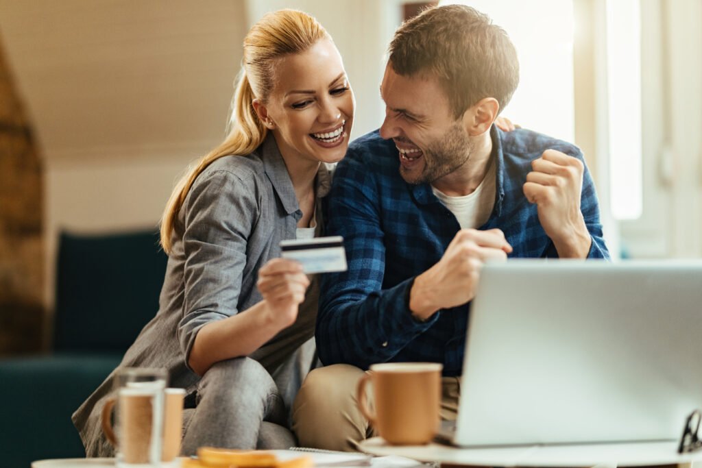 Happy couple celebrating while using credit card and online banking at home.